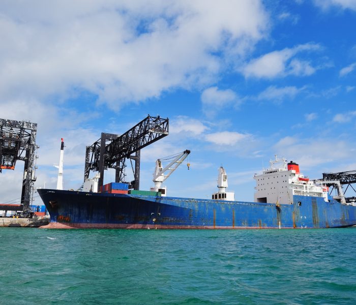 Cargo ship at Miami harbor with crane and blue sky over sea.